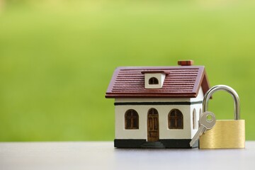 Home security. House model, key and padlock on white table outdoors, closeup. Space for text