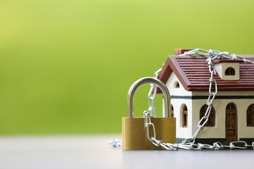 Home security. House model, chain and padlock on light table outdoors, closeup. Space for text