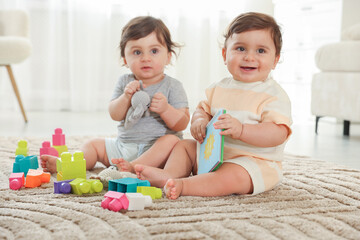 Cute little twin babies playing with toys on floor at home