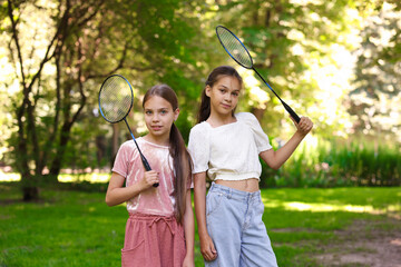 Portrait of smiling little girls with badminton rackets in park