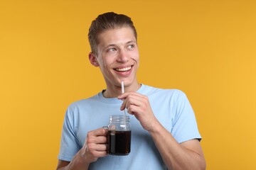 Happy man with mason jar of refreshing soda drink on yellow background