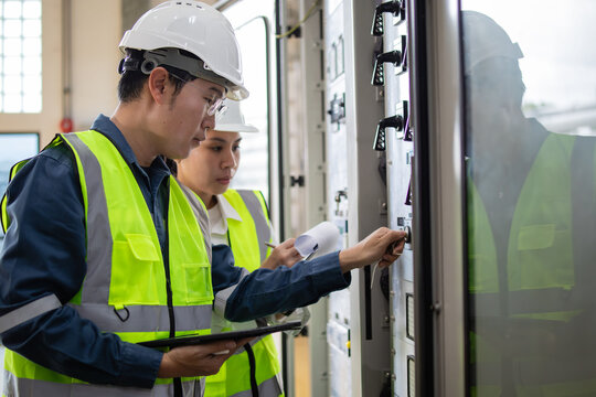 Engineers Performing Maintenance Check on Electrical Control Panel in Industrial Setting with Safety Gear