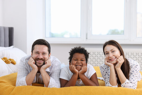 Adoption. Happy parents and their son on bed at home