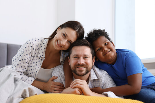 Adoption. Happy parents and their son on bed at home