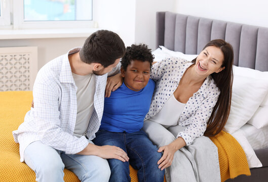 Adoption. Happy parents and their son on bed at home