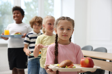 Little kids with trays of tasty food in school canteen, selective focus