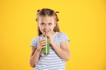 Little girl drinking juice through straw on orange background