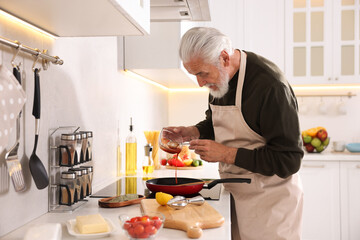 Elderly man cooking dish on cooktop in kitchen