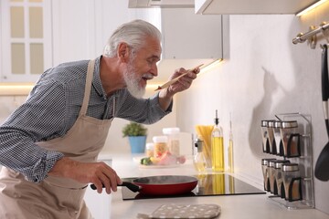 Elderly man cooking dish on cooktop in kitchen