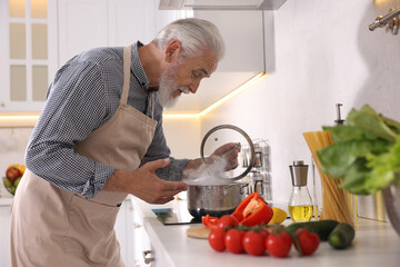 Elderly man cooking dish on cooktop in kitchen
