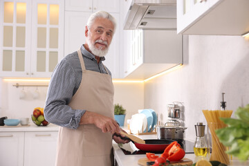 Elderly man cooking dish on cooktop in kitchen