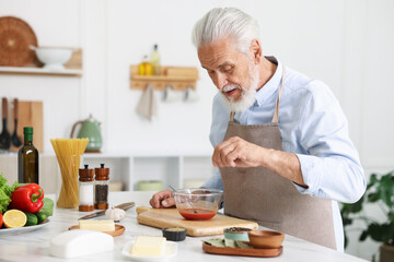 Elderly man cooking at white marble table in kitchen