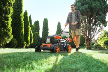 Man cutting green grass with lawn mower in garden, low angle view