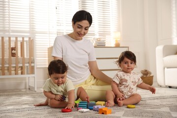 Fototapeta premium Mother with her cute little twins and toys on floor at home