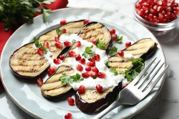 Slices of grilled eggplant with pomegranate seeds and yoghurt on white marble table, closeup