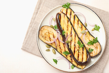 Slices of grilled eggplant, parsley, pumpkin seeds and onion on white table, top view. Space for text