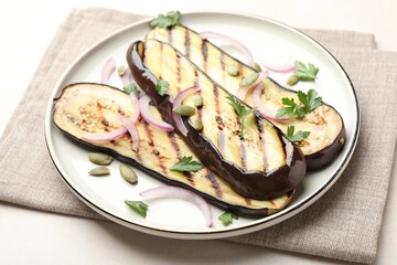 Slices of grilled eggplant, parsley, pumpkin seeds and onion on white table, closeup