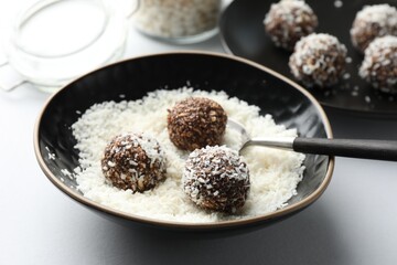 Making tasty chocolate candies with nuts and coconut flakes at white table, closeup