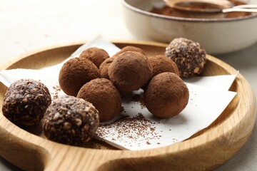 Tasty chocolate candies with cocoa powder on light table, closeup