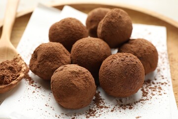 Tasty chocolate candies with cocoa powder and spoon on light table, closeup