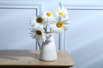 Beautiful chamomile flowers in vase on wooden table near grey wall