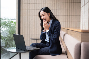 Surprised businesswoman reacting with excitement while looking at laptop in office.