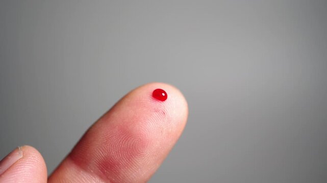 A close-up shot of a single drop of blood on the tip of a human finger