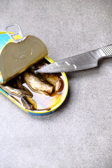 Sprats in tin can on grey textured table, top view. Steel knife
