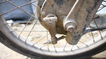 Closeup of a rusty, weathered motorcycle rear wheel hub and brake system, showcasing aged metal,...