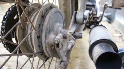 Closeup of a rusty, weathered motorcycle rear wheel hub and brake system, showcasing aged metal,...