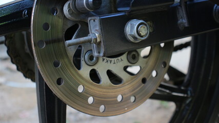 Closeup of a motorcycle rear disc brake system with visible rotor, caliper mount, and axle...