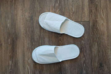A pair of slippers on wood floor. Top view white slippers.