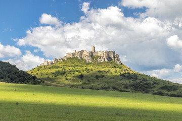 Spis Castle in Slovakia, Europe. Historic castle atop a verdant hill under a cloudy blue sky,...
