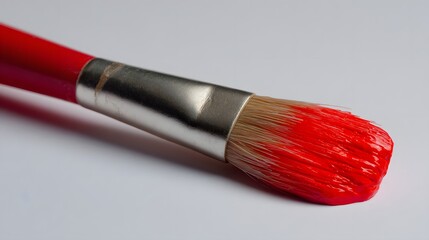 Close-up of a red paintbrush with vibrant crimson paint, showcasing the brushstrokes and bristles against a plain white backdrop.