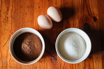 Top view of cocoa powder, sugar and eggs on wooden table, baking ingredients concept.