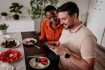 Couple enjoying a home-cooked meal and sharing moments on a smartphone at their dining table