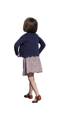 Fillette vue de dos qui  marche, portant une robe à motifs fleuris, gilet bleu marine et chaussures rouges, cheveux châtains au carré, bras en mouvement, tenue printanière
