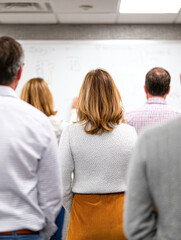 A group of people attentively observes a presentation in a classroom setting, focusing on a whiteboard with notes and illustrations.