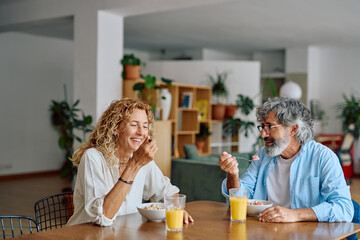 Cheerful senior couple laughing and enjoying a healthy breakfast together at home, sharing moments of joy and connection in their bright kitchen