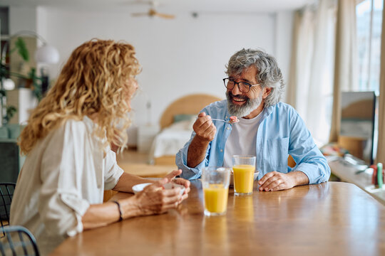 Smiling senior couple enjoying breakfast together at the dining table, sharing joyful conversations and love in the bright morning light - Powered by Adobe