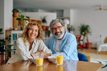 Smiling elderly couple holding hands while having breakfast at home, enjoying a healthy meal and each other's company