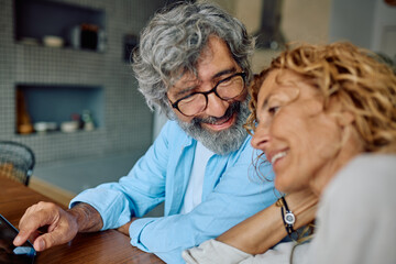 Smiling senior couple enjoying time together while browsing on a digital tablet in their bright, modern kitchen filled with warmth