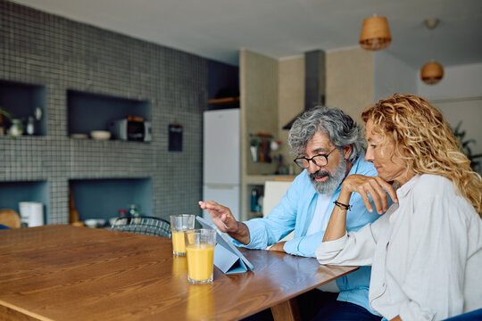 Senior couple enjoying breakfast together in a modern kitchen, using a digital tablet to browse the internet and connect online
