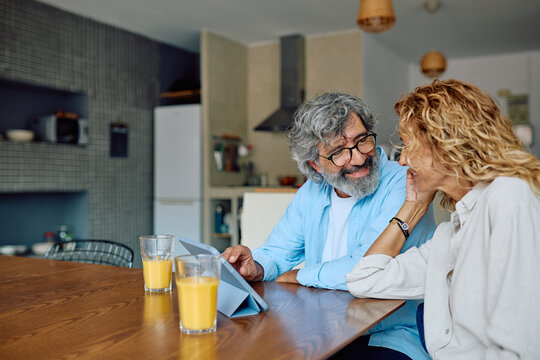 Cheerful mature couple sharing a delightful breakfast while browsing the internet on a digital tablet in their modern kitchen