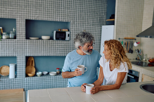 Happy mature couple drinking coffee and chatting in modern kitchen, enjoying their retirement together at home - Powered by Adobe