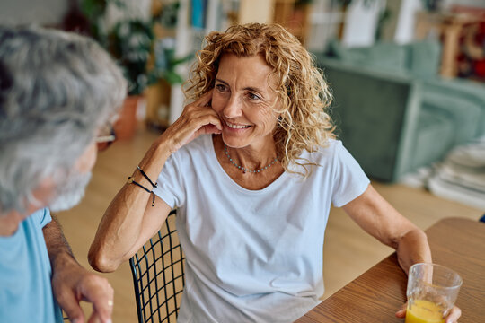 Happy senior woman enjoying breakfast at home, listening to her husband while sharing smiles and engaging in warm conversation together