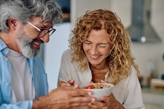 Senior couple laughing and enjoying a nutritious breakfast of oatmeal together in their cozy kitchen, celebrating love and happiness