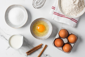 Baking ingredients flat lay with flour, eggs, sugar, and spices on marble surface