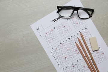 Student passing exam. Answer sheet, pencils, eraser and glasses on wooden table, flat lay. Space...