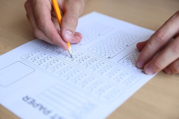 Naklejka premium Student filling out multiple choice test at wooden table, closeup. Passing exam